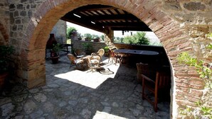 Terrassa exterior amb paviment de pedra, un arc de maó, mobiliari de vimet i zona de barbacoa.