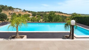 A swimming pool with a clear view of the surrounding landscape, including trees and distant buildings. - Villa Raggera - Private villa with pool near Noto (Ispica)