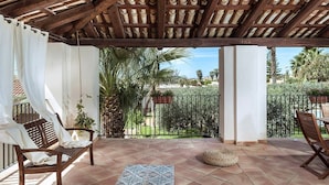 A covered patio with a wooden bench, a woven pouf, and a tiled floor. - Casa Maissala Due, with shared pool near sea (Marsala)
