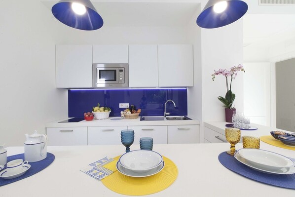 Une cuisine moderne avec des armoires blanches, un four à micro-ondes encastré et un pare-feu éclairé en bleu.