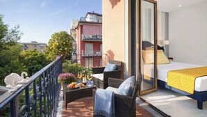 A balcony with wicker furniture, a bed with a yellow bedspread, and a view of neighboring buildings.