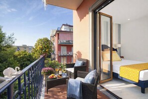 Un balcon avec des meubles en osier, un lit recouvert d’une couvre-lit jaune et une vue sur les bâtiments voisins.