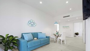 Een moderne woonkamer met een blauwe bank, witte stoelen, een glazen tafel en een decoratief wandobject.