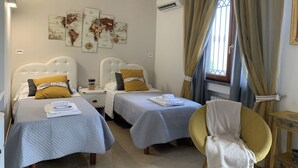 Habitación de hotel con dos camas, una silla, una mesita y una ventana con cortinas.
