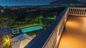 Un balcón con vistas a una piscina y al horizonte urbano al anochecer.