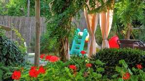 Un jardín con cerca de madera, un parque infantil y diversas plantas y flores.