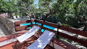 Une terrasse en bois avec une piscine, entourée d’une végétation luxuriante et de murs en pierre.