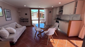 Un espace de vie compact comprenant un canapé, une table à manger en verre et un coin cuisine.