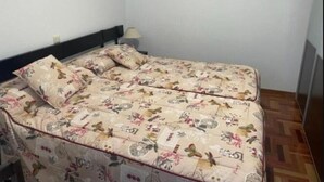 Ein schlichter, kleiner Raum mit einem Bett, ausgestattet mit einer blumigen Tagesdecke und passenden Kissen.