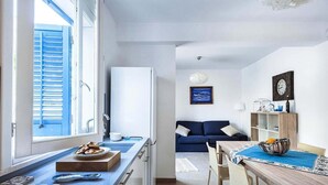 Eine kleine Küche mit einem Gasherd, einem Kühlschrank und einem Fenster mit blauen Fensterläden.
