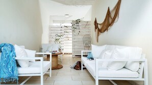 Ein helles, weißes Wohnzimmer mit einer weißen Couch, zwei weißen Sesseln, einem kleinen runden Tisch und einer Hängematte an der Wand.