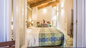Un dormitorio con techo de madera, una cama con colcha, una mesa y una silla, y un radiador.