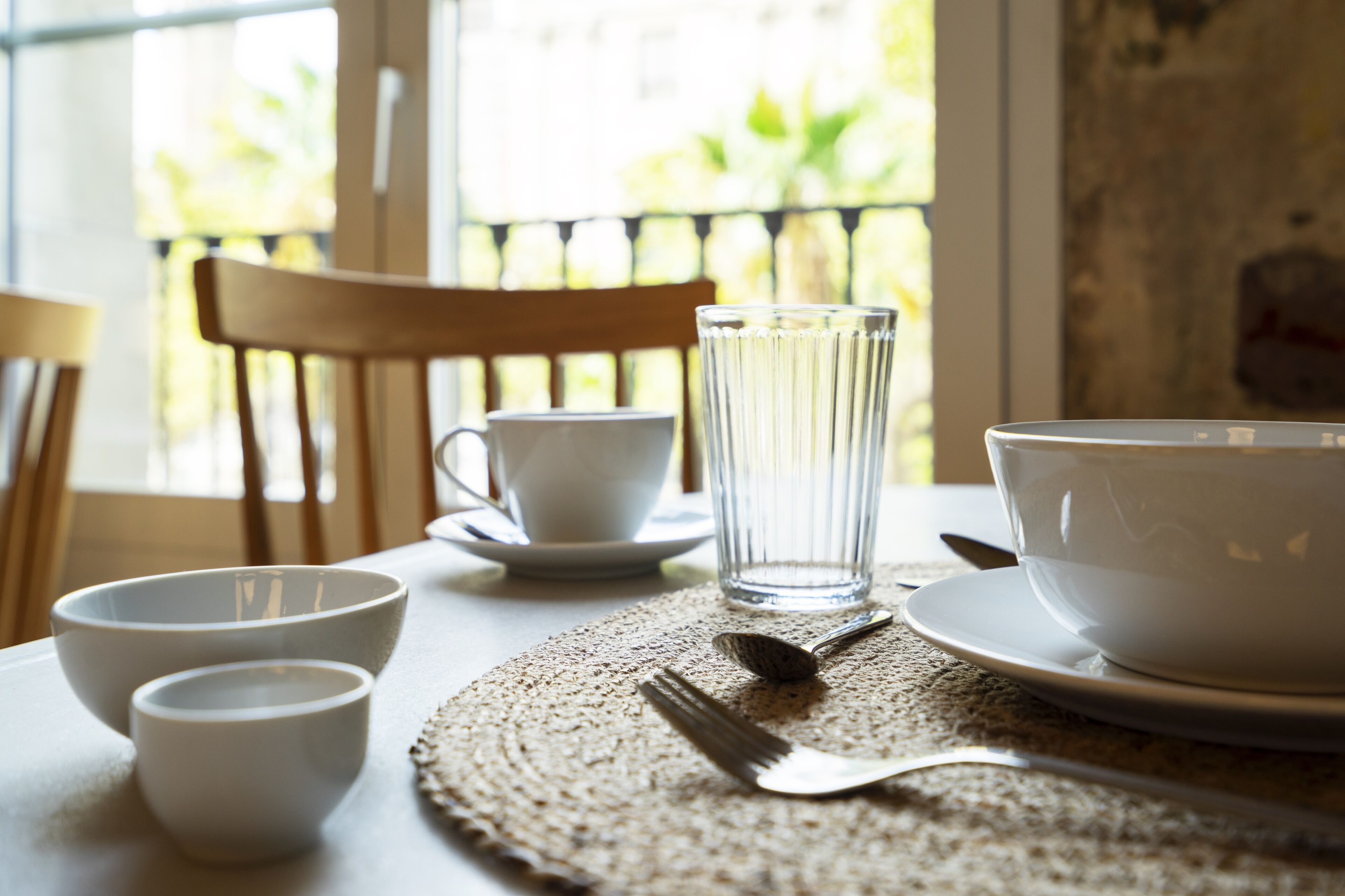 A dining table with white bowls, a glass, and cutlery.