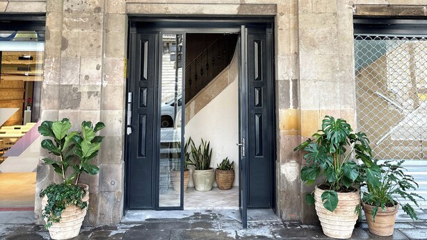 A building entrance with a stone facade, arched windows, and potted plants. - Porxos Garden (Barcelona)