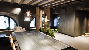 A modern interior with a long wooden table, hanging pendant lights, and a large window with a view. - Porxos Garden (Barcelona)
