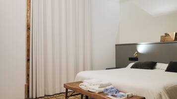 Habitación de hotel con cama, mesita de noche con toallas, cabecero con luz y suelo estampado.