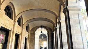 An arched corridor with stone columns and a hanging light fixture. - Porxos Garden (Barcelona)