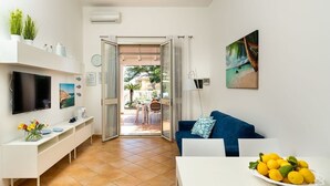 A modern living room with a TV, a dining area with a table and chairs, a sofa with cushions, and a balcony with a view of the outdoors. - Corrado Residence  - Private villa with independent apartments (Reitani)