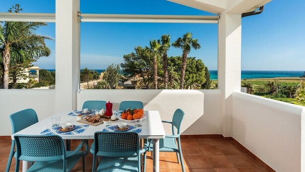 A dining area with a table set for two, overlooking a coastal landscape with palm trees and the sea. - Corrado Residence  - Private villa with independent apartments (Reitani)