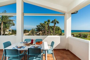 Un coin repas avec une table dressée pour deux personnes, offrant une vue sur un paysage côtier avec des palmiers et la mer.