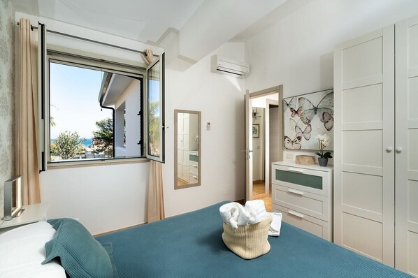 Une chambre à coucher avec un lit, une fenêtre, un miroir, une commode et une armoire.