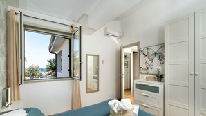 A bedroom with a bed, a window with curtains, a dresser, a mirror, and an air conditioning unit. - Corrado Residence (Blu) - Apartment near Marzamemi (Reitani)