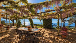 Une terrasse extérieure avec une table et des chaises, entourée de verdure et offrant une vue sur la mer.