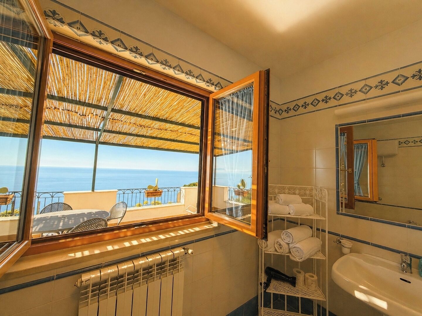 A bathroom with a view of the sea, a radiator, a sink, and a mirror.