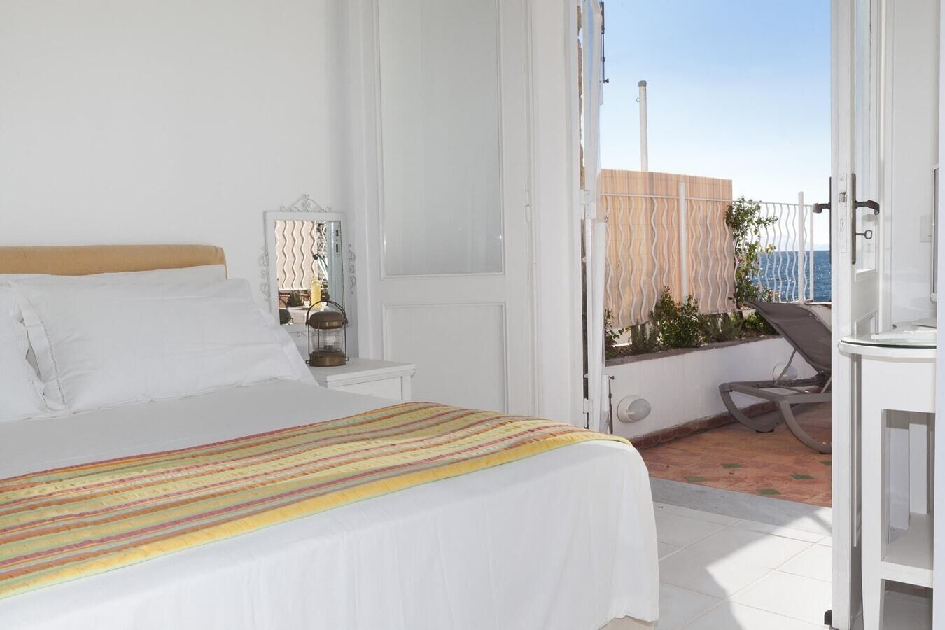 Ein Schlafzimmer mit Bett, Nachttisch, Lampe und Blick auf den Balkon.