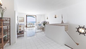 A spacious living area with a white sofa, a coffee table, and a TV. There is a wooden bookshelf and a decorative wall piece. - Villa Mia - Sea front private villa close to town (Napoli)