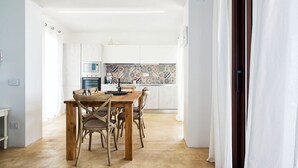 Et moderne køkken med hvide skabe, et flisebeklædt bagpanel og et spiseområde med et træbord og stole.