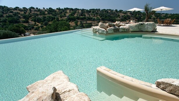 A clear swimming pool with rock formations and lounge chairs, surrounded by a hilly landscape. - Ragusa Apartments (Grigio) - apartment near Ragusa (Ragusa)