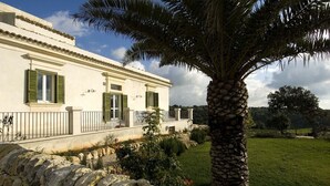 A two-story house with a stone wall in front, a palm tree, and a grassy yard.