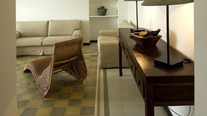 A living room with a sofa, a chair, a table with lamps, and a shelf with decorative items.