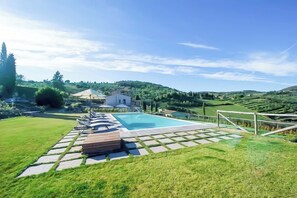 A swimming pool with lounge chairs, a grassy area, and a house in the background.