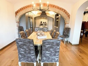 A dining area with a long wooden table, upholstered chairs, and a brick archway.
