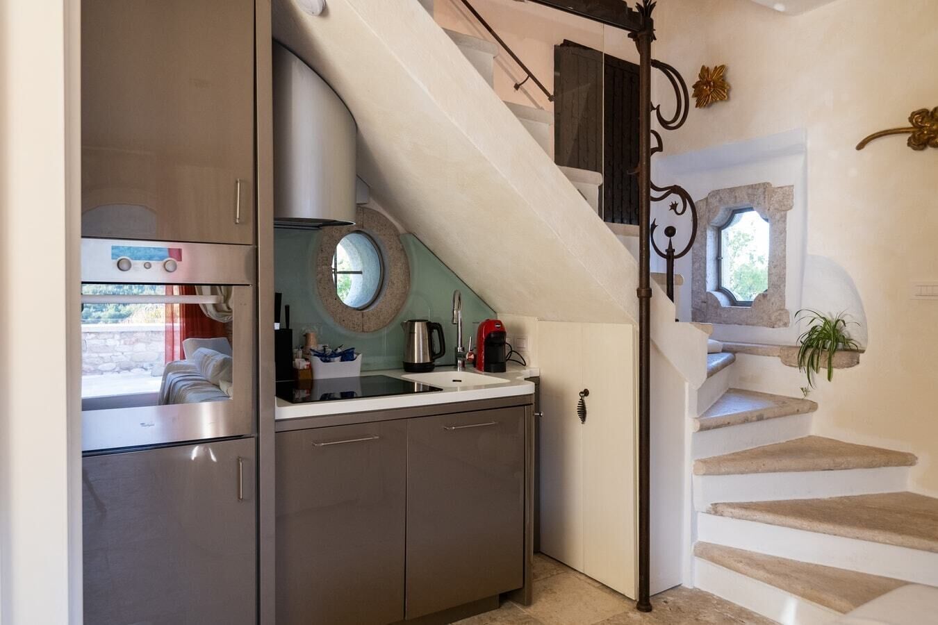 A compact kitchen with a sink, a coffee maker, and a round mirror.