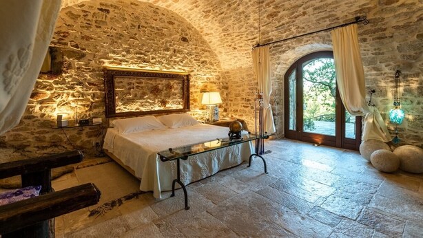 Une chambre aux murs de pierre, avec un lit, des lampes de chevet et une vue sur l’extérieur.