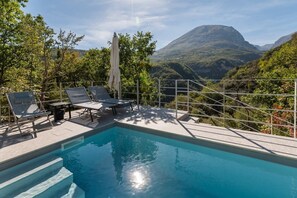 Zona de piscina con sillas de descanso y vistas a un paisaje montañoso.