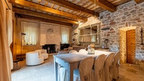 Un coin repas rustique avec un mur en pierre, des poutres en bois, une cheminée et une table à manger dressée pour six personnes.