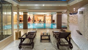 A luxurious indoor pool area with a glass ceiling, marble flooring, and elegant seating arrangements.
