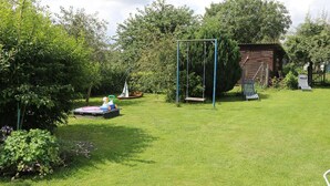 A grassy outdoor area with a swing set, a small play structure, and a wooden shed.