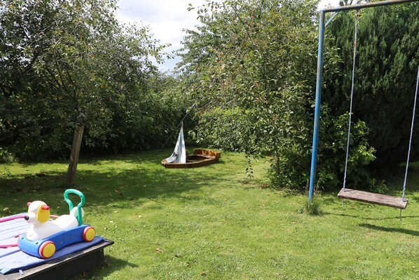 A grassy backyard with a swing set, a small boat, and a toy duck.