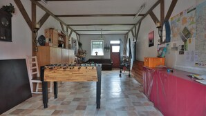 Habitación amplia con mesa de futbolín, sofá y una mesa roja con papeles.