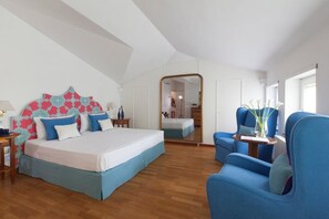 Ein Schlafzimmer mit einem großen Bett, einem blauen Sessel, einem Spiegel und Blick in einen anderen Raum.