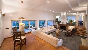 A spacious living area with a sofa, dining table, and chairs, large windows with a view, and a fireplace.