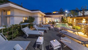 A rooftop pool area with lounge chairs and a small table, surrounded by a stone wall and plants.
