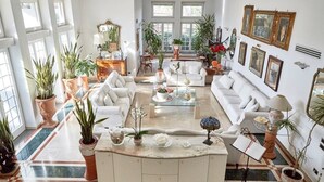 A spacious living room with a marble coffee table, white sofas, and potted plants.