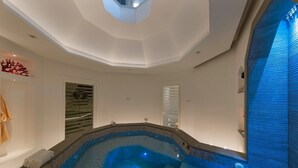 A modern spa room with a large, geometrically shaped hot tub, a ceiling with recessed lighting, and a wall-mounted towel rack.