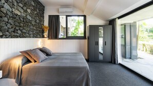 Une chambre moderne avec un mur en pierre, un lit avec des oreillers, une armoire et une grande fenêtre.